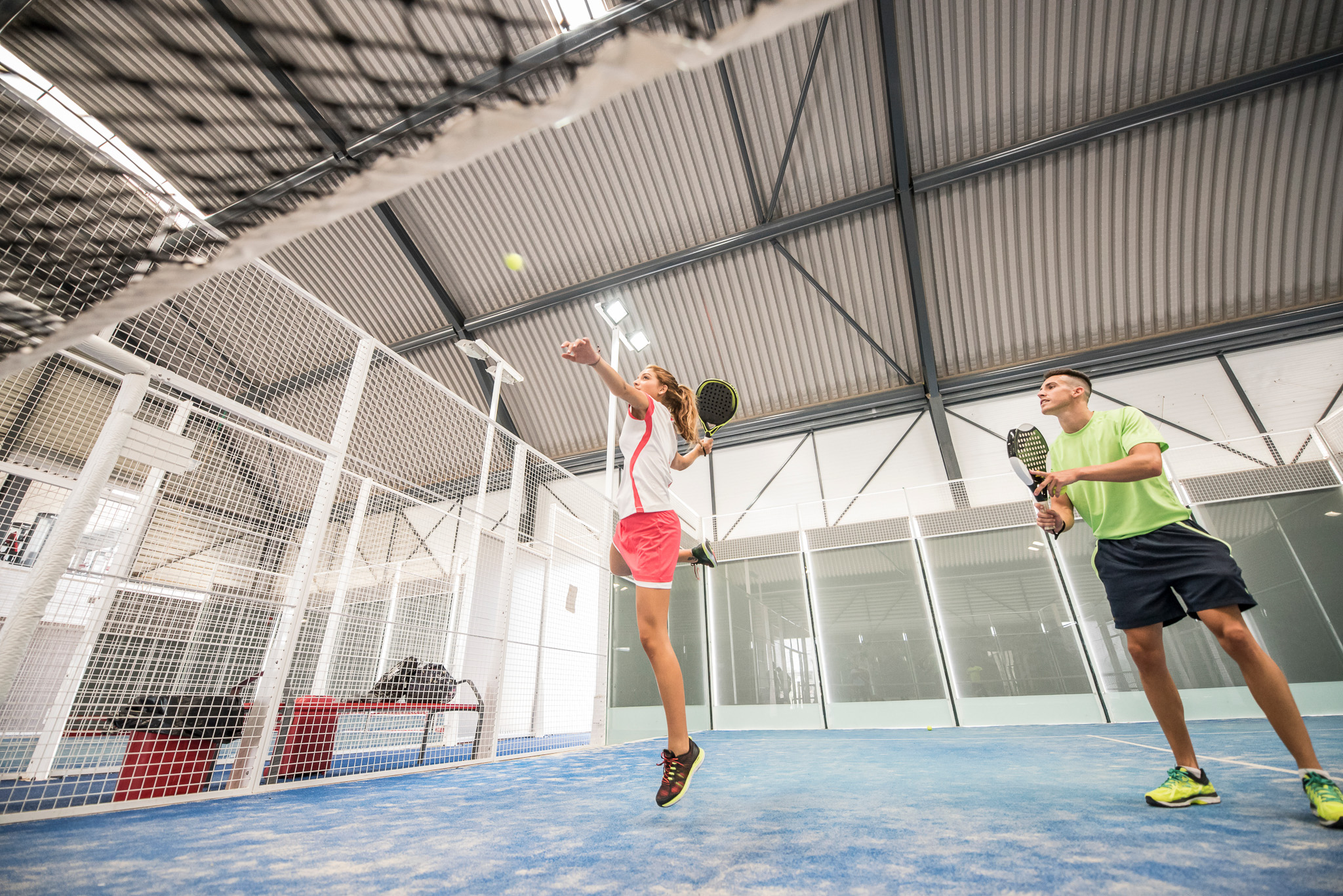 Woman hits ball at indoor padel court. Discover how to reduce noise in padel courts 